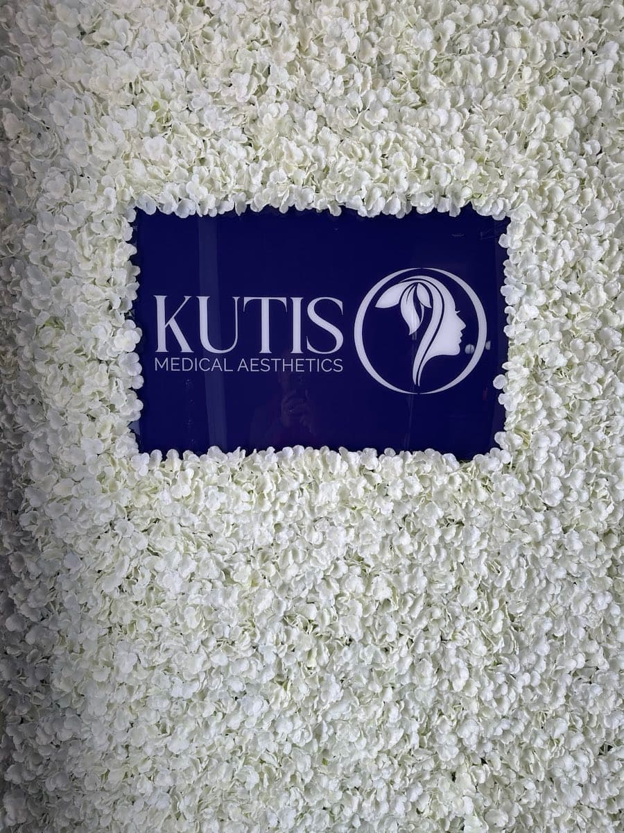 The Kutis Medical Aesthetics sign, mounted on a wall of white flowers inside the practice